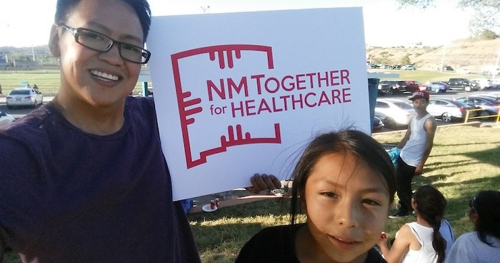 Un padre y su hijo sostienen un cartel de NM Juntos por la Sanidad