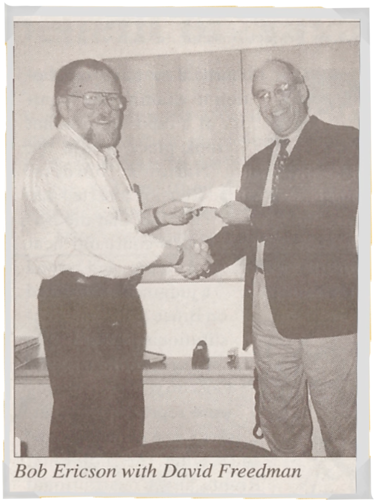Fotografía antigua de dos hombres dándose la mano y sosteniendo un trozo de papel entre ellos.